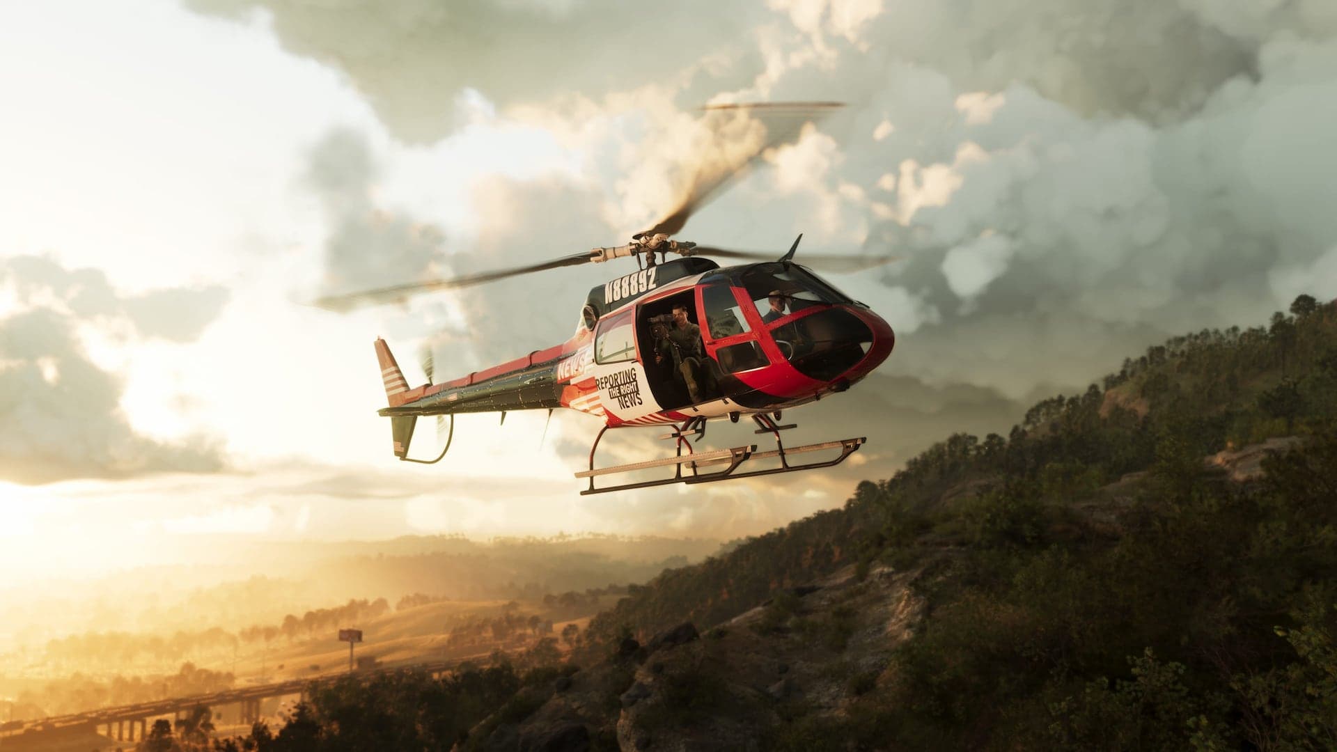A red and white news helicopter banking over a forested ridge at sunrise, a camera operator visible in the open door.